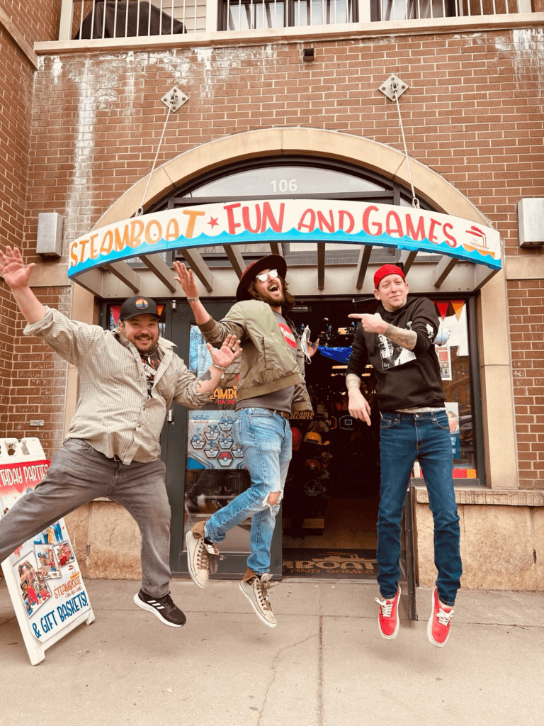 Three guys jumping in front of the Steamboat Fun and Games store