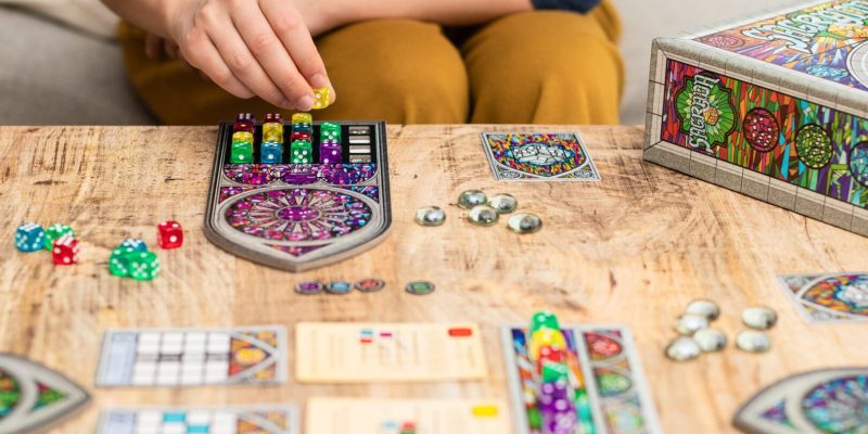 Hand placing yellow die on stained-glass board game